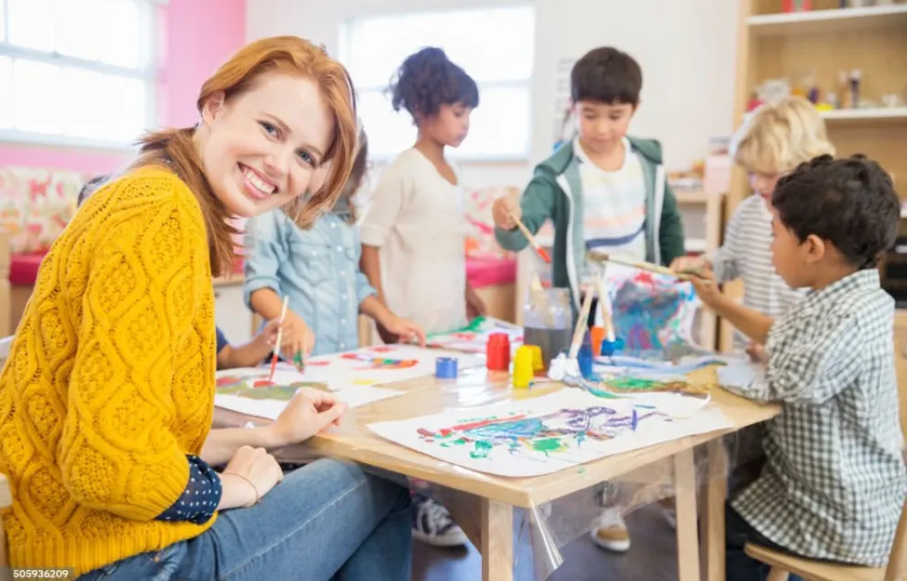 Person sitzt an einem Tisch zusammen mit Kindern und lächelt